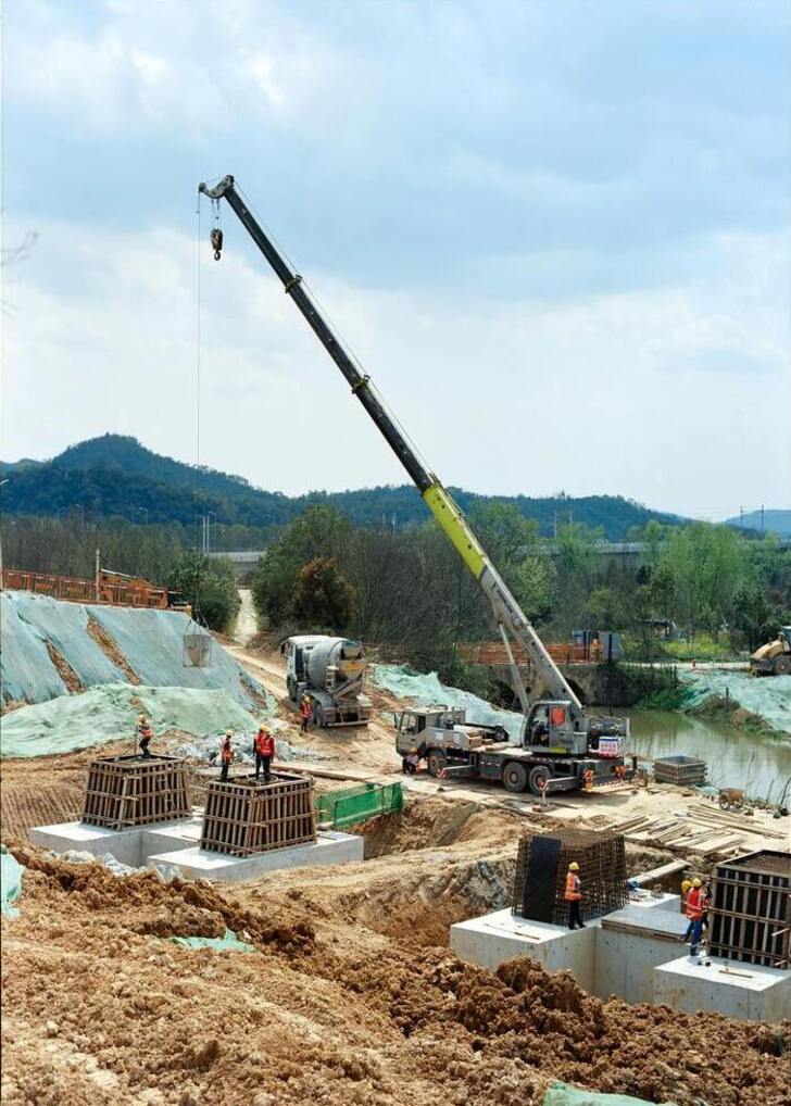 A wide view of an active construction site in Mumbai, India, with numerous workers, heavy machinery, and progress on steel erection and concrete pouring under a clear sky.