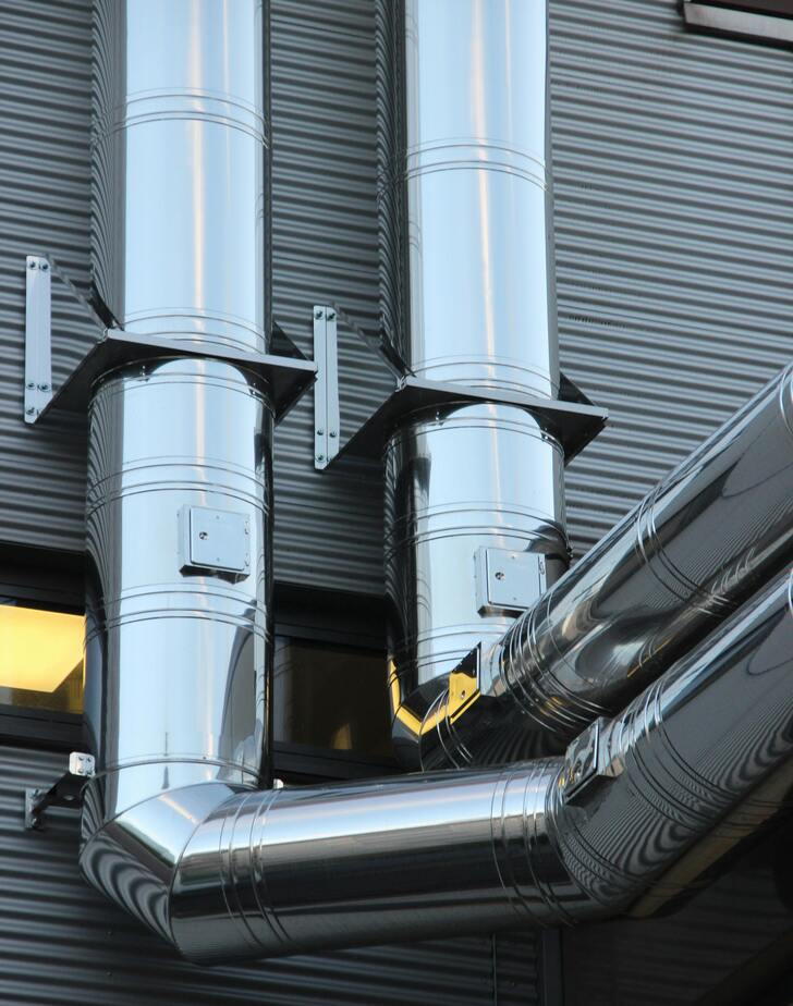 A close-up of a complex network of insulated ductwork and chilled water pipes in an industrial mechanical room.